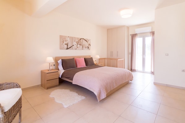 A bedroom with a bed, nightstands, a dresser, a crib, and a large window with curtains.