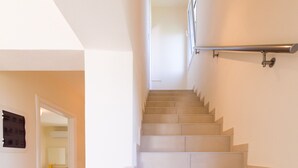 Una scala con corrimano e una porta sul fondo che dà su una stanza con uno specchio e un tavolino.