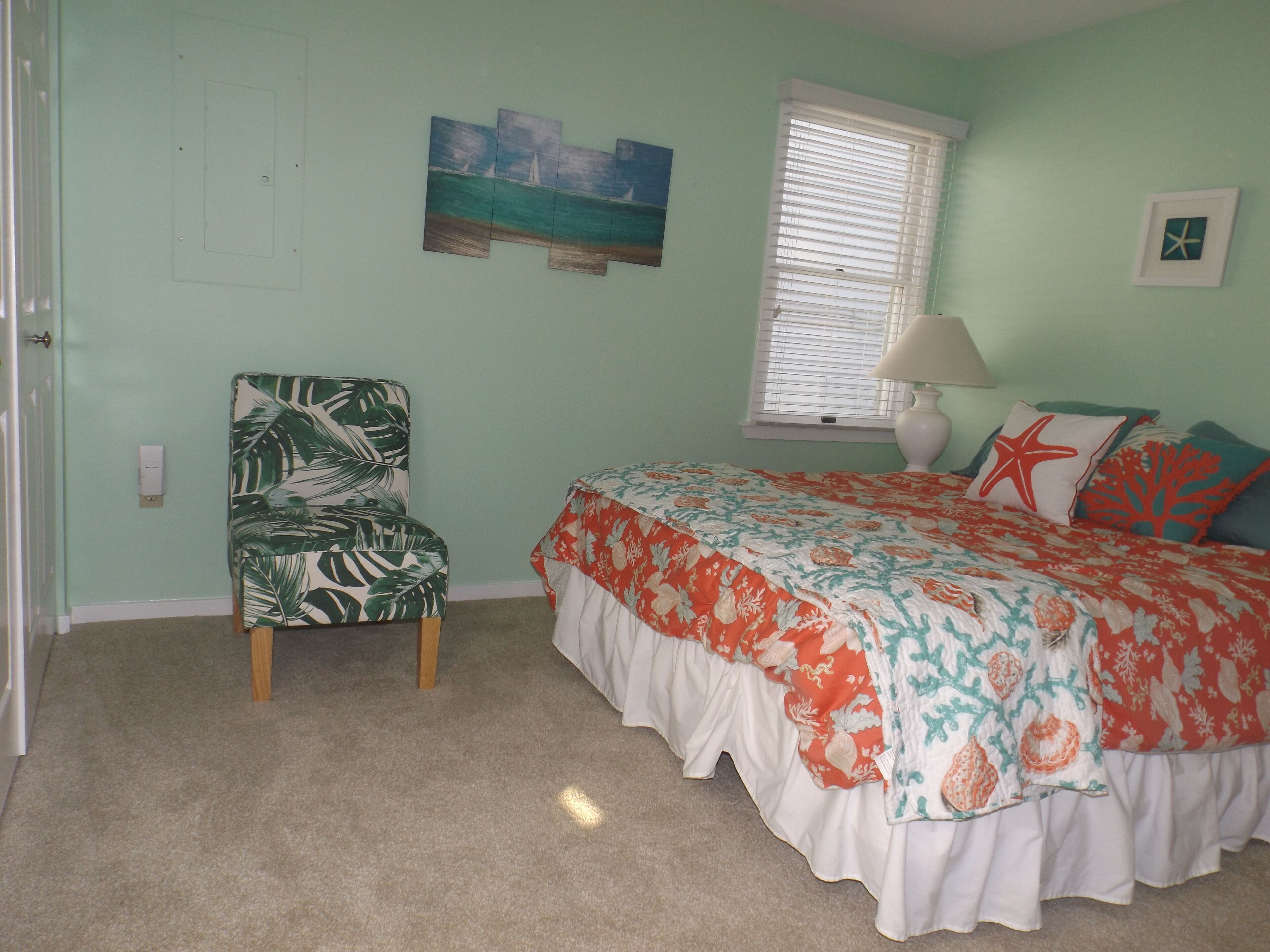 A bedroom with a bed, a chair, a window with blinds, and a wall with a painting.