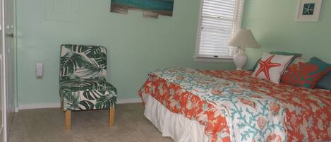 A bedroom with a bed, a chair, a window with blinds, and a wall with a painting.