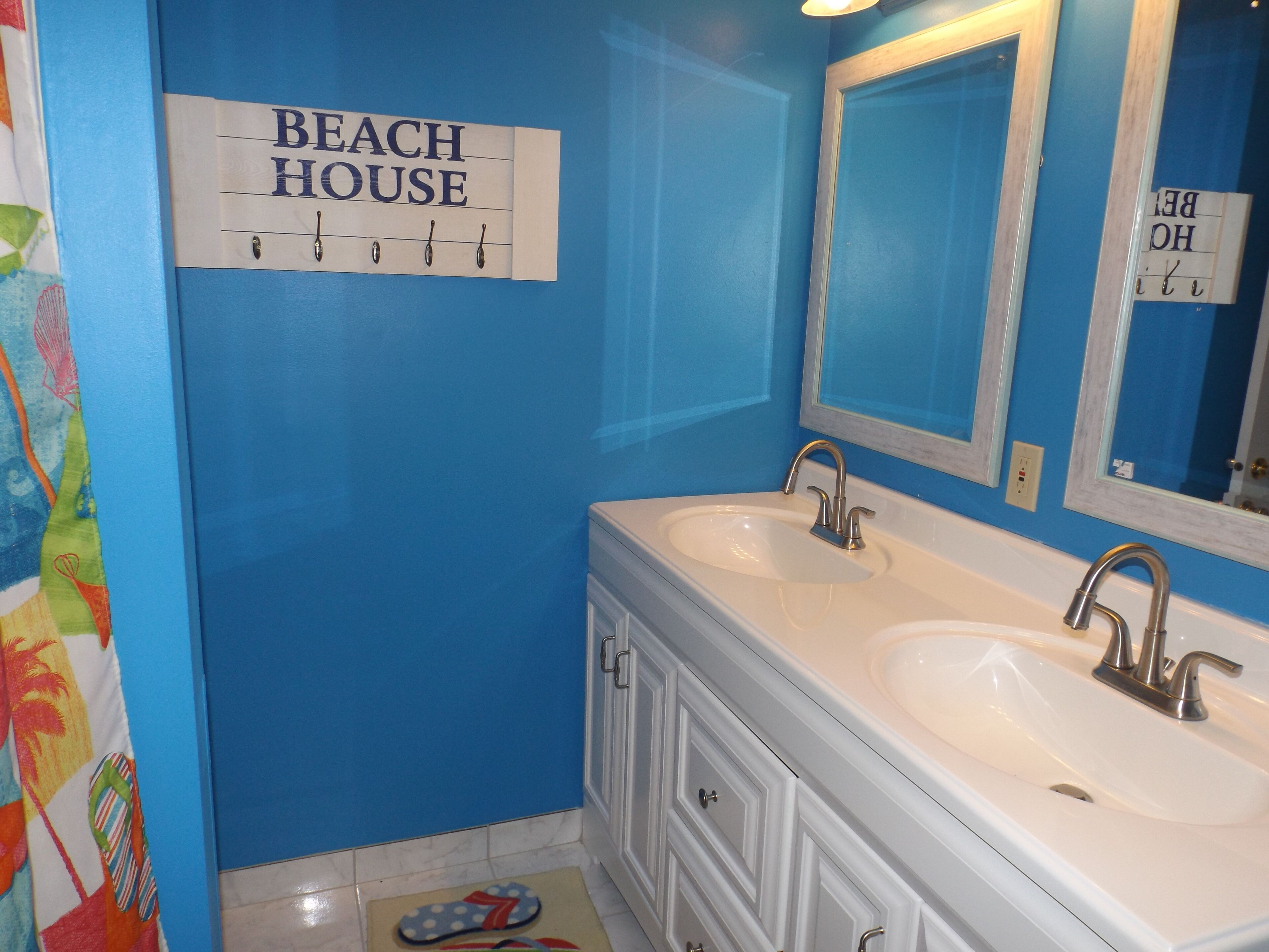 A bathroom with two sinks, a mirror, and a sign that reads 'BEACH HOUSE'.