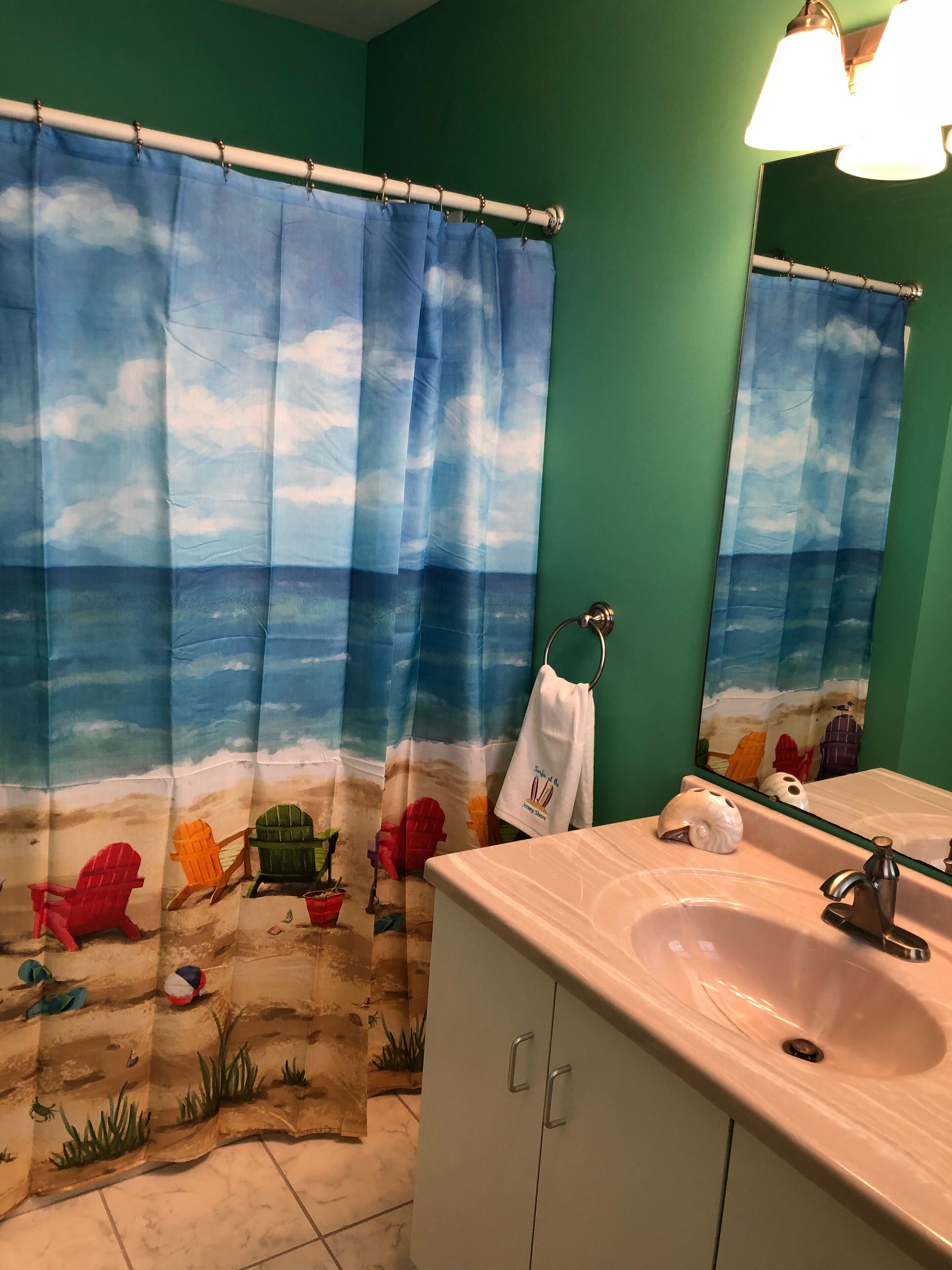 Un baño con cortina de ducha de temática playera, un lavabo y un espejo.