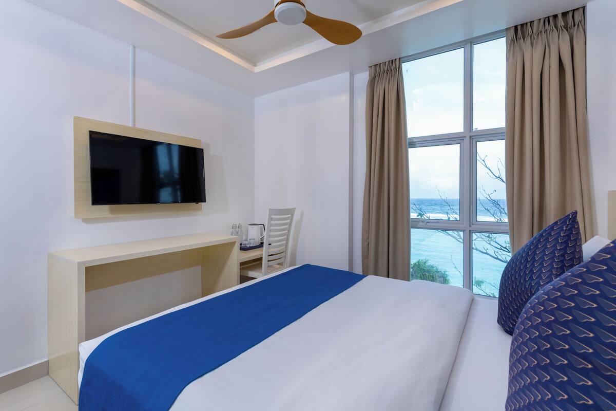 A hotel room with a bed, a desk, a television, and a window with curtains.