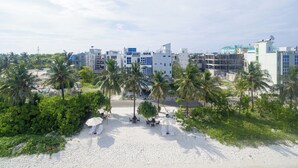 A beachside hotel with white buildings, palm trees, and a sandy beach with sun loungers. - The White Harp Beach Hotel (Hulhumalé)