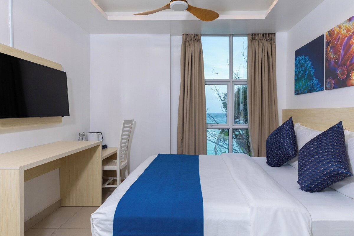 Habitació d'hotel amb llit, escriptori, televisió, ventilador de sostre i finestra amb cortines.