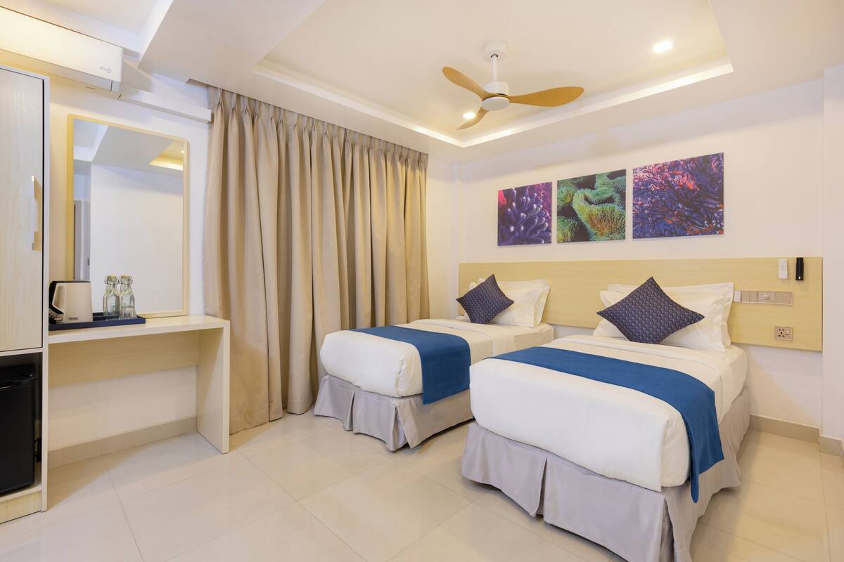 A hotel room with two beds, a desk, a mirror, and a ceiling fan.