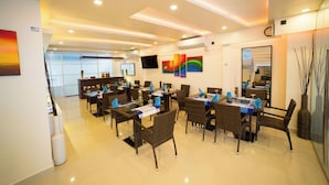 A hotel dining area with multiple tables, chairs, and a television screen. - The White Harp Beach Hotel (Hulhumalé)