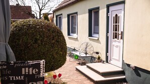 A pathway leading to a house with a white door, a small garden with red flowers, and a metal chair outside. - Sunny 4-star holiday home in Stralsund, the gateway to the island of Rügen (Stralsund)