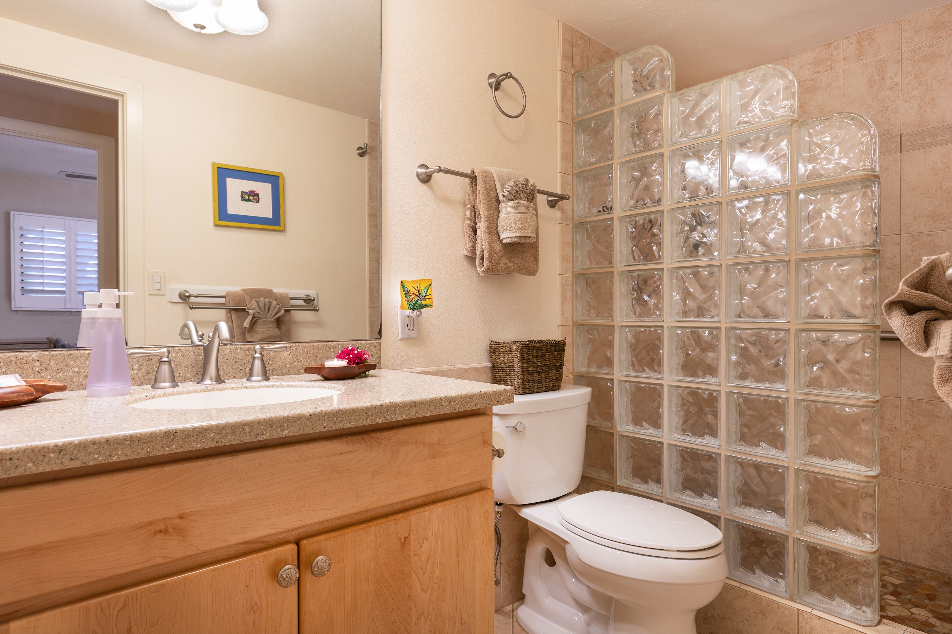 A bathroom with a sink, mirror, toilet, and shower with frosted glass panels.