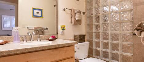A bathroom with a sink, mirror, toilet, and shower with frosted glass panels.