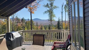 Une terrasse couverte, dotée d’une table et de chaises, qui offre une vue sur un paysage montagneux aux couleurs automnales.