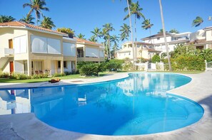 A swimming pool with a curved edge, surrounded by palm trees and modern buildings with balconies.