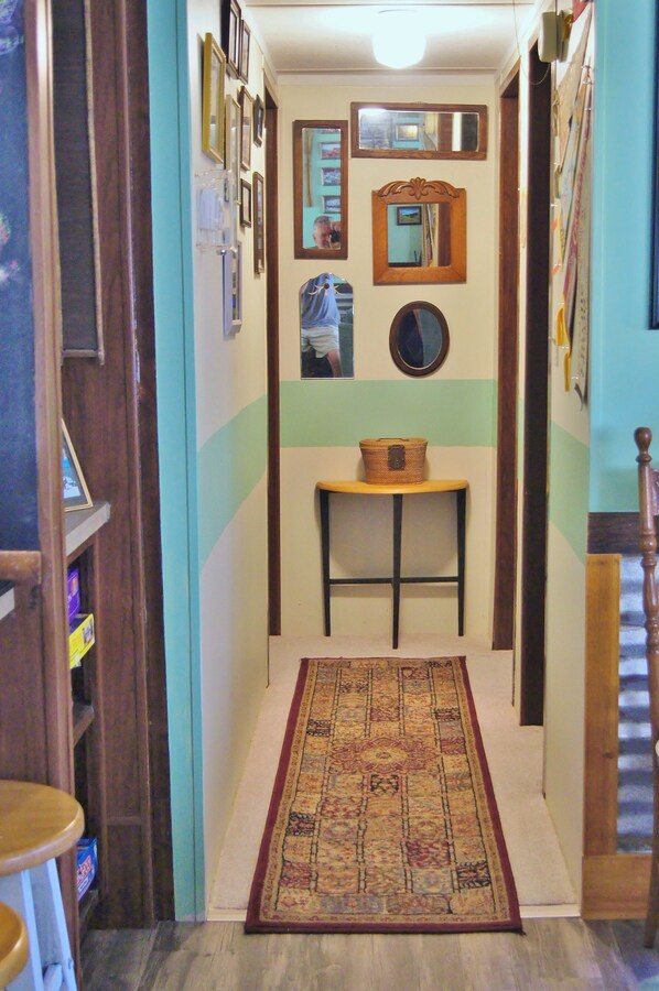A narrow hallway with a patterned rug, a small table with a basket, and several framed mirrors on the walls.