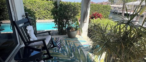 Uma área de estar coberta ao ar livre, com espreguiçadeiras e piscina ao fundo.