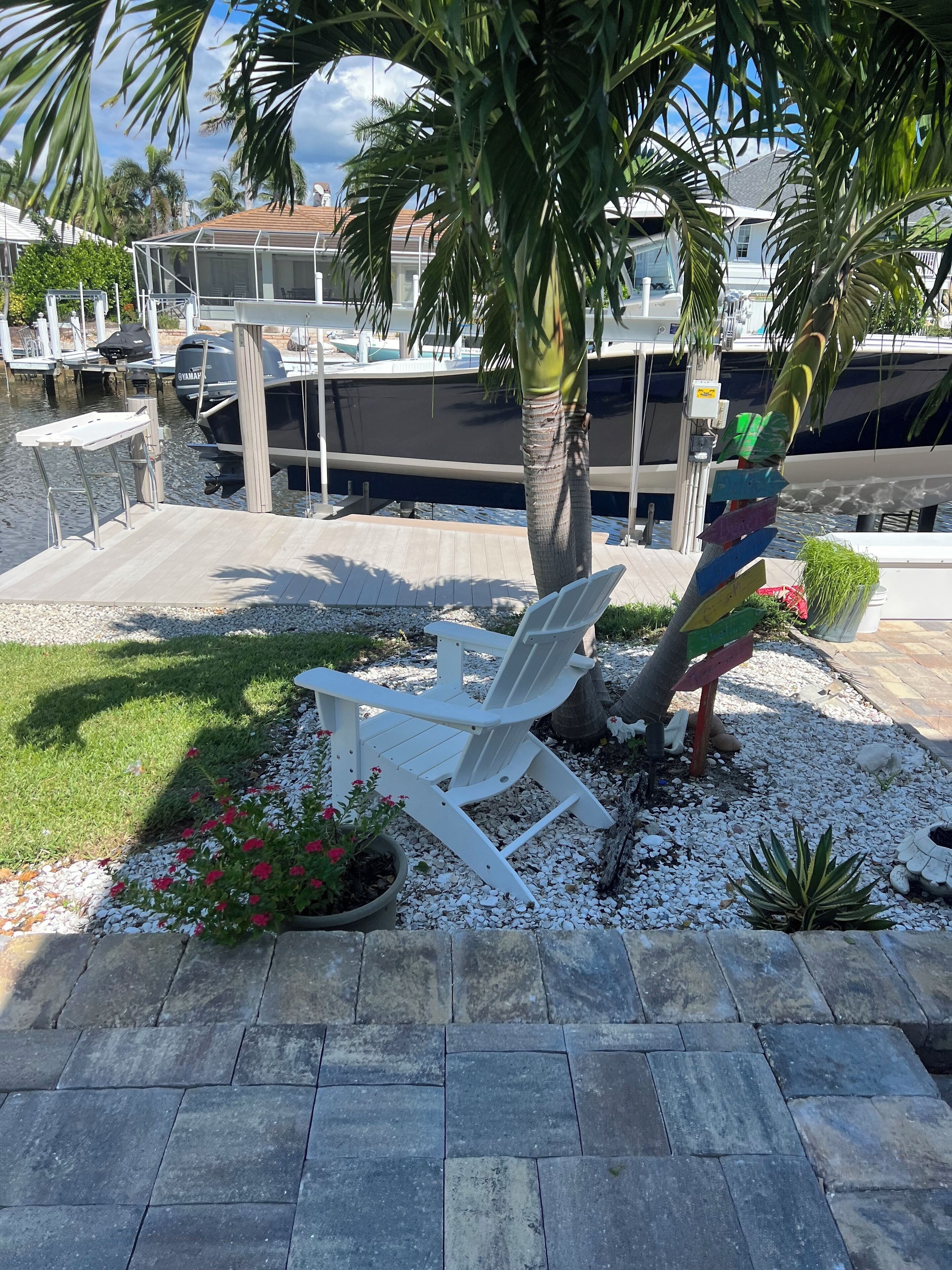 Un puerto deportivo con barcos amarrados, una silla lounge blanca, una palmera y una jardinera decorativa con follaje.