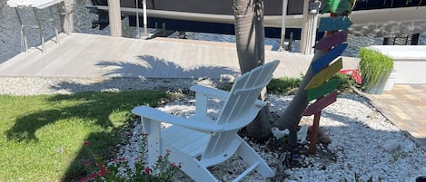 Un puerto deportivo con barcos amarrados, una silla lounge blanca, una palmera y una jardinera decorativa con follaje.