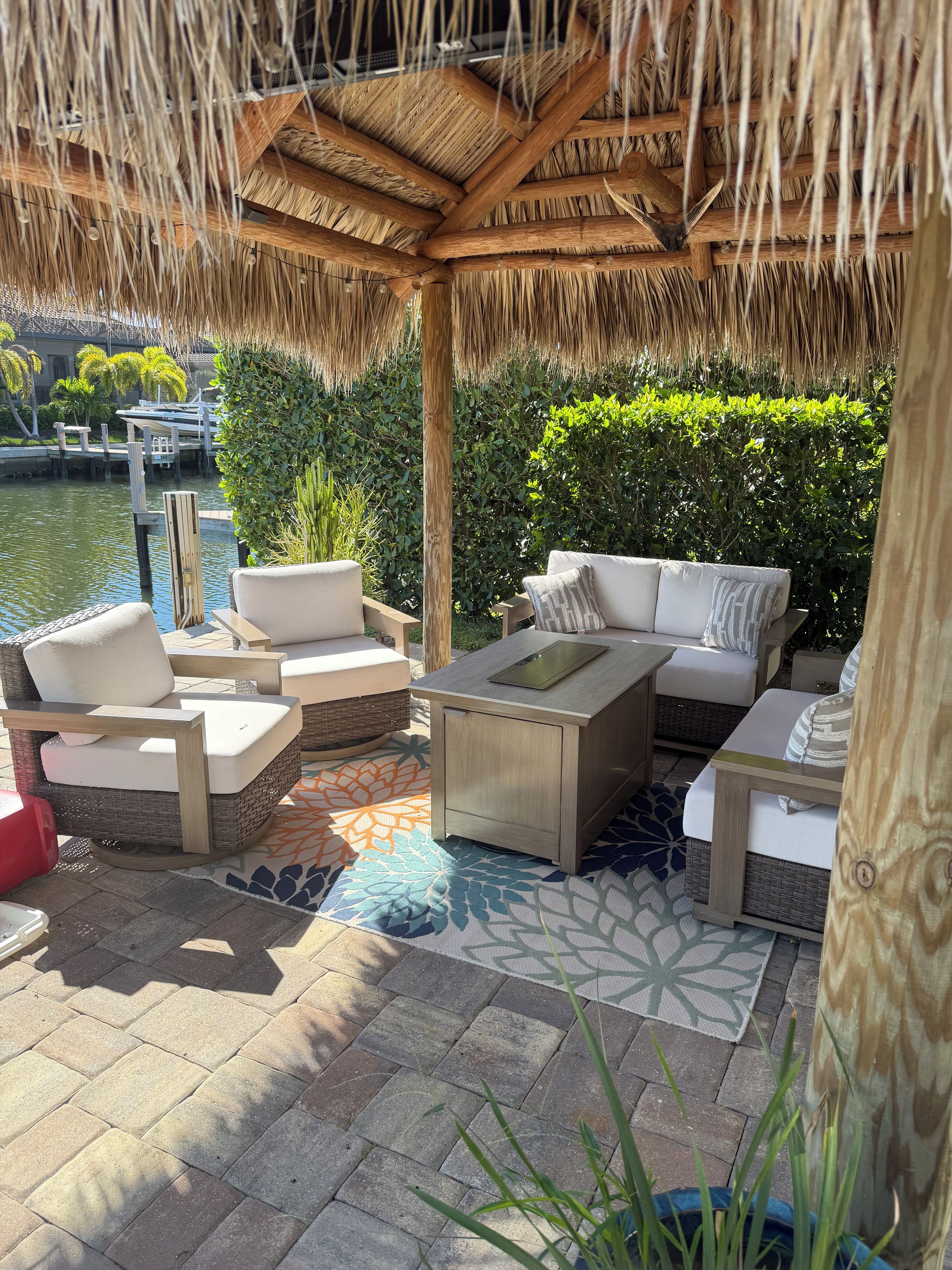 An outdoor seating area with wicker furniture and a wooden table, overlooking a body of water.