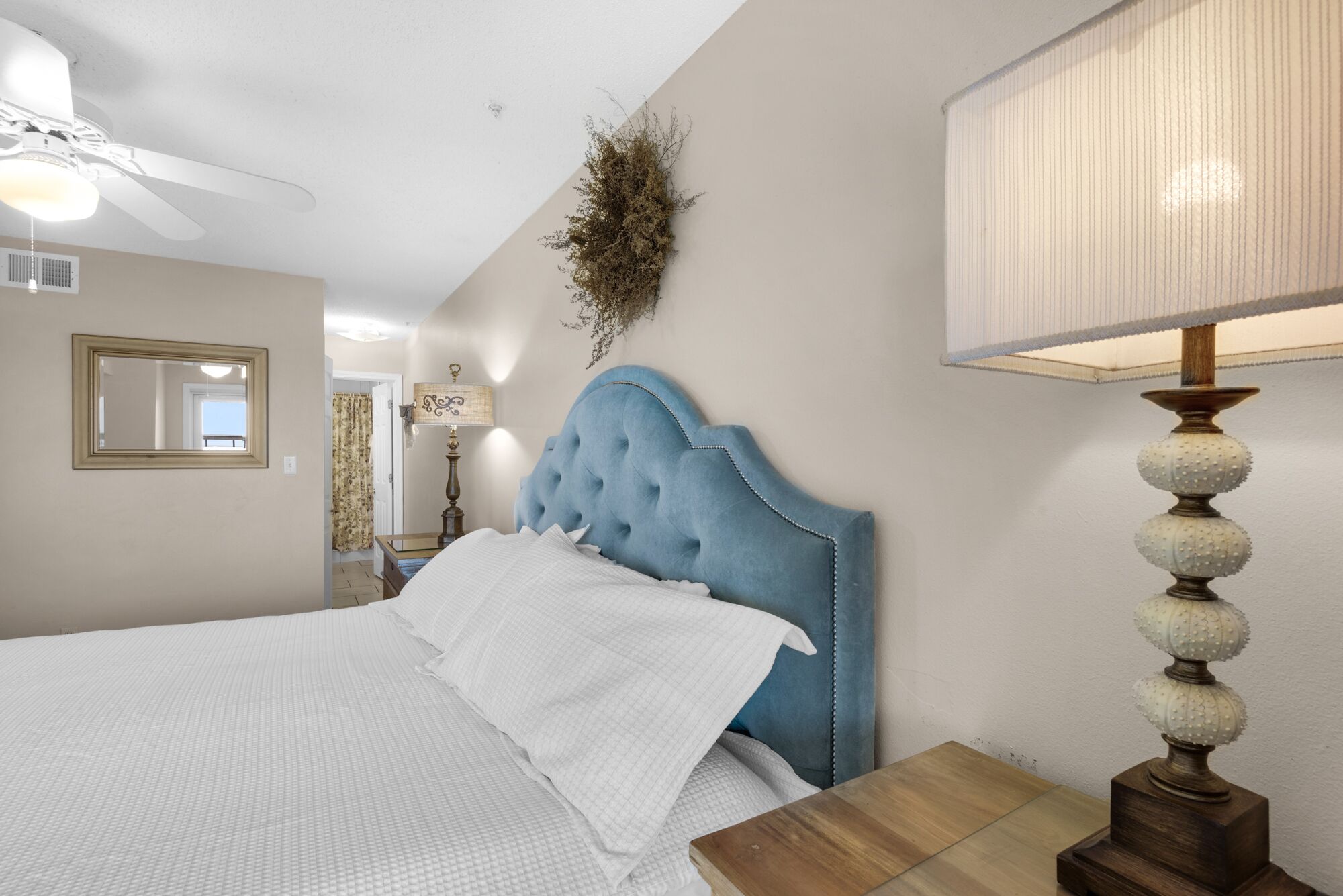 Een slaapkamer met een bed, een plafondventilator, een wandlamp en een spiegel.