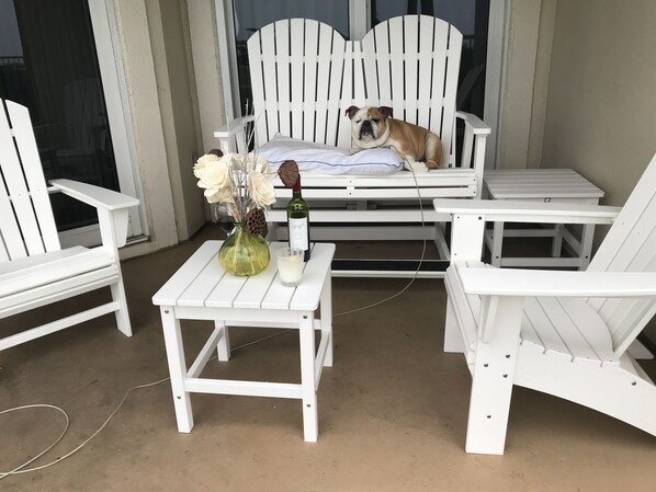 A white outdoor seating area with a dog on a bench, a table with a vase and candle, and chairs. - Perfect location! Ground floor, 40 Steps to Pool or Beach! Pets Welcome! (Miramar Beach)