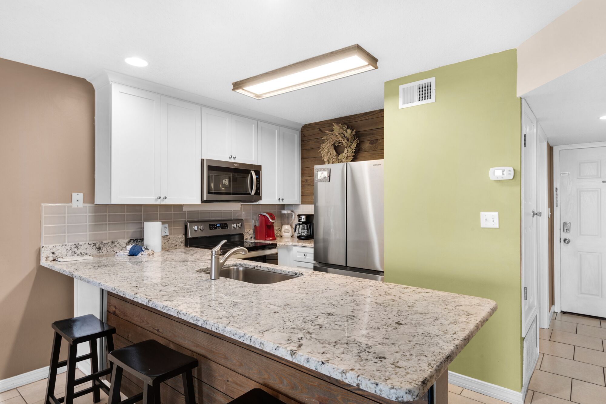A modern kitchen with white cabinets, a stainless steel refrigerator, a built-in microwave, and a granite countertop.