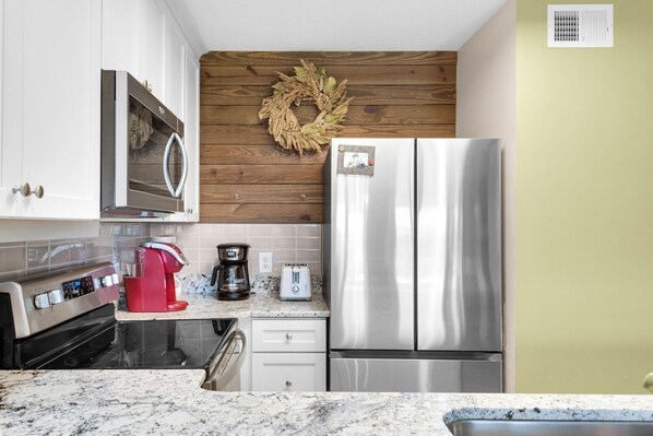 A kitchen with white cabinets, a stainless steel refrigerator, a coffee maker, and a microwave.