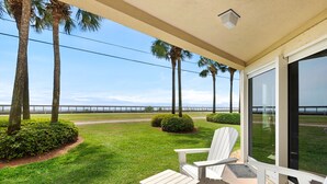 A covered outdoor area with two Adirondack chairs, a small table, and a view of the beach and a bridge. -  Perfect location! Ground floor, 40 Steps to Pool or Beach! Pets Welcome! (Miramar Beach)