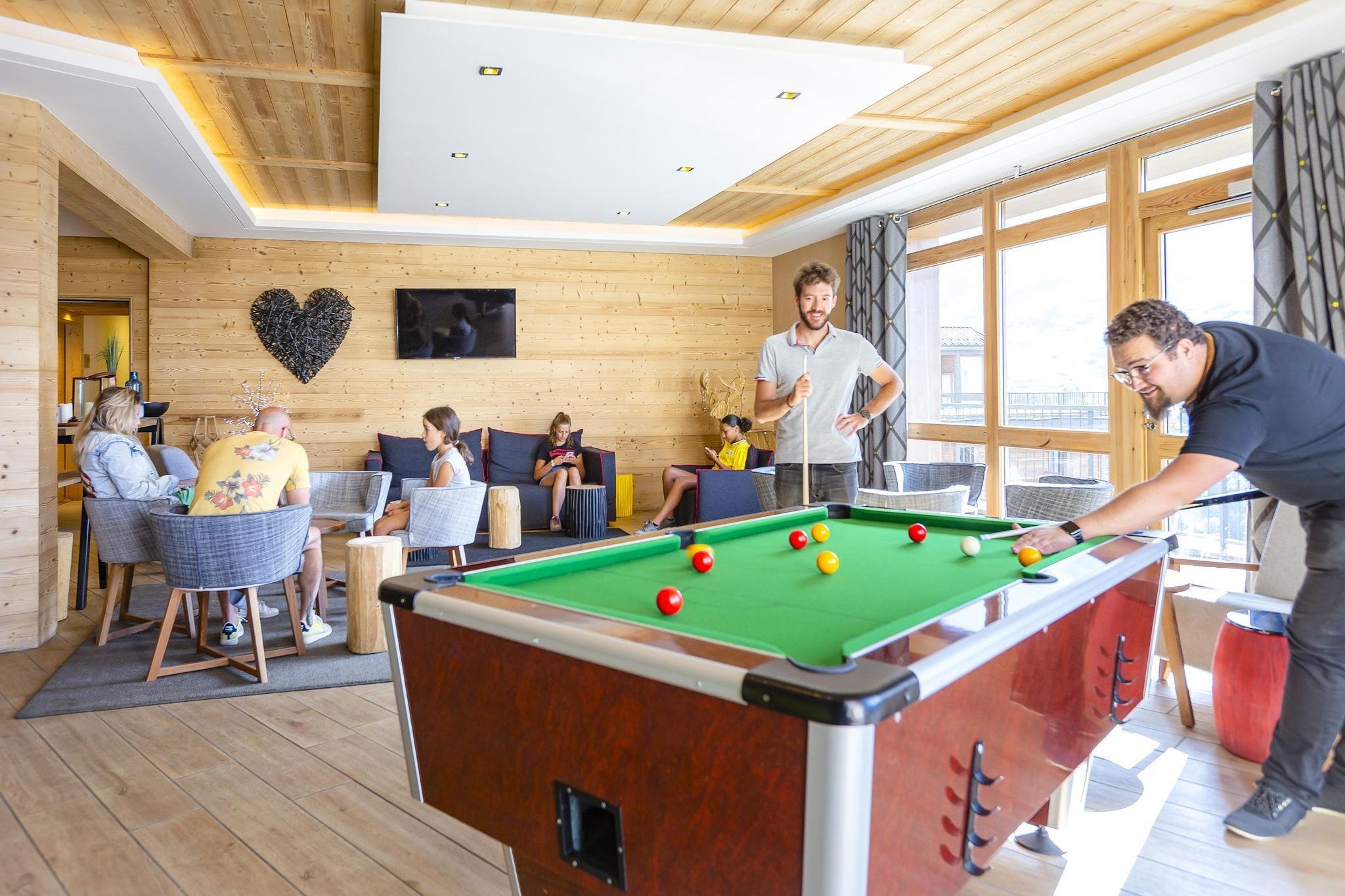 A pool table in a room with wooden walls and large windows.