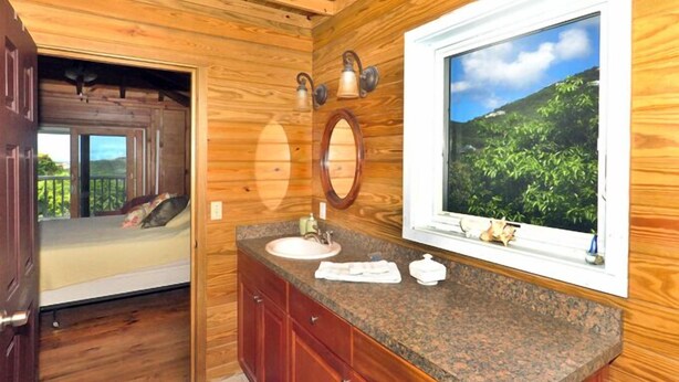A wooden cabin-style bathroom with a sink, mirror, and window overlooking greenery. - Fish Tales a Caribbean Cottage style home with a Pool, walk to Reef Bay Beach (St John)
