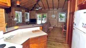 A wooden cabin kitchen with a refrigerator, wooden cabinets, a dining area with chairs, and a ceiling fan. - Fish Tales a Caribbean Cottage style home with a Pool, walk to Reef Bay Beach (St John)
