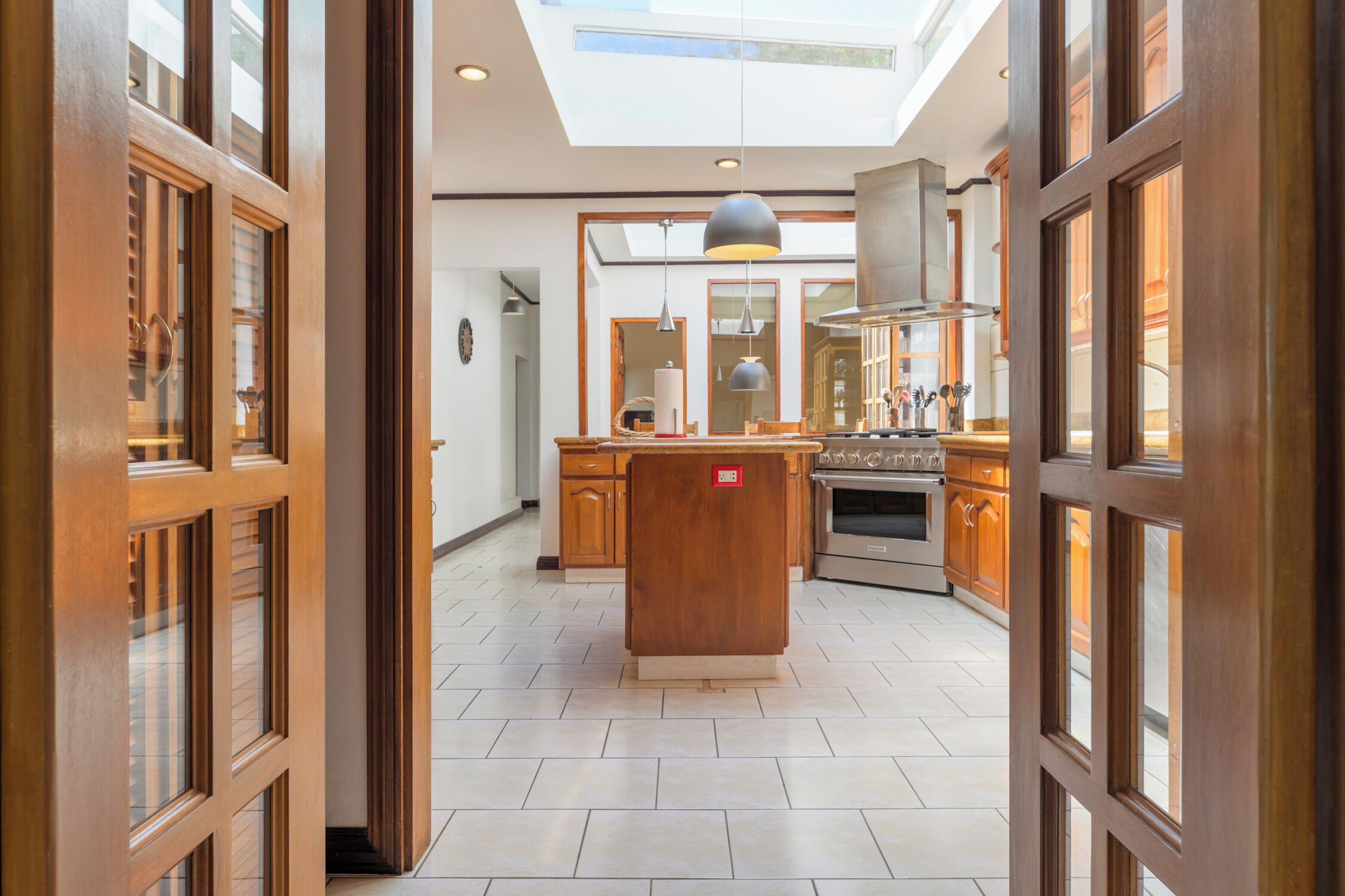 A modern kitchen with a central island, wooden cabinetry, and a skylight above.