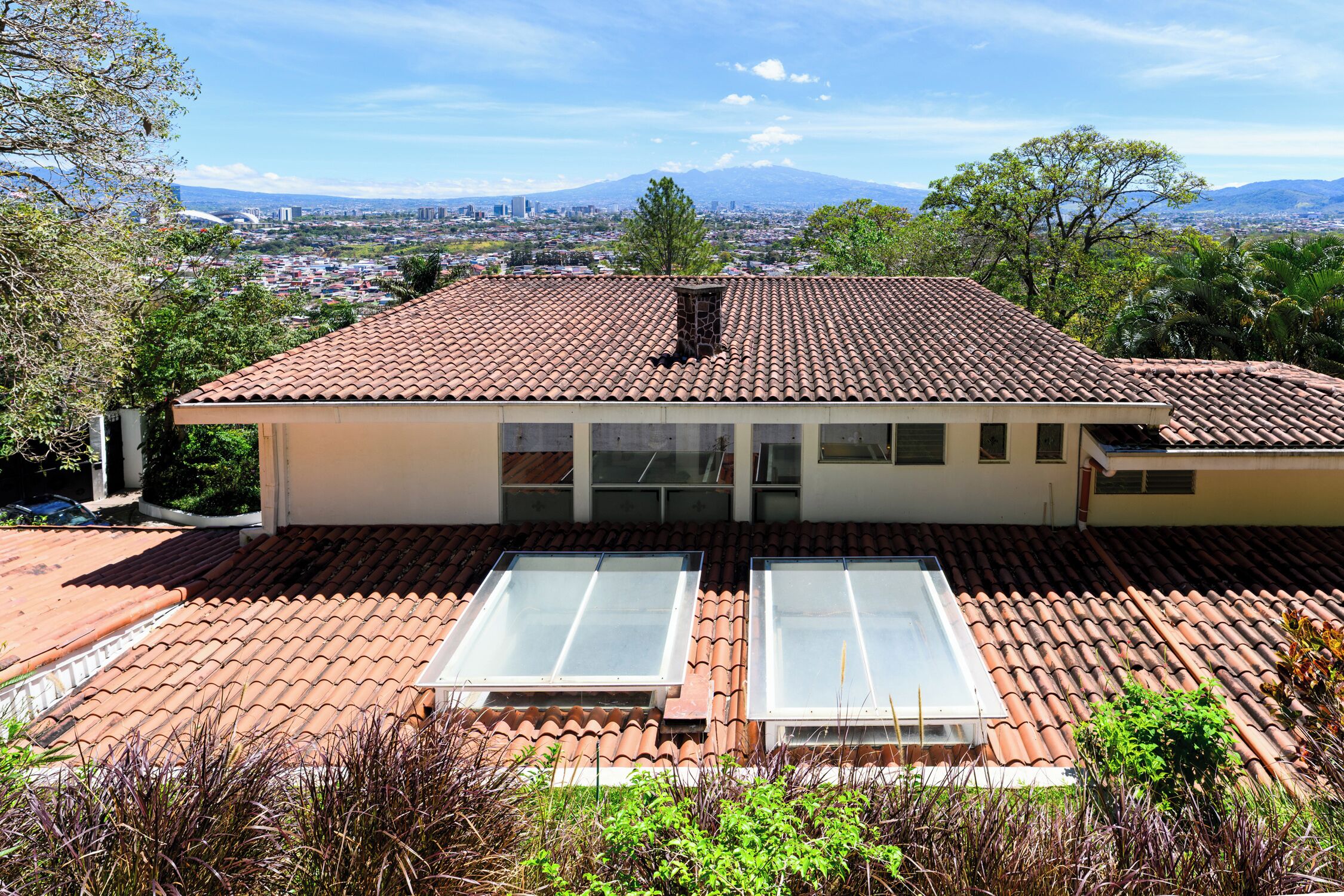 A two-story building with a tiled roof, a flat roof with a skylight, and a view of a cityscape and mountains in the background.