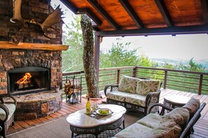 Une cheminée en pierre avec un feu de bois, du mobilier d’extérieur et une vue sur le paysage.