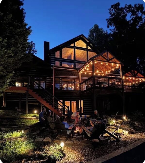 A multi-level wooden cabin with a deck and string lights, surrounded by a landscaped garden.