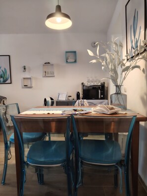 Ein Essbereich mit einem Holztisch, blauen Stühlen, einer Hängeleuchte und einer Wandvase mit weißen Blumen.