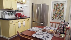A compact kitchen with yellow cabinets, a stainless steel refrigerator, and a dining table set with a patterned tablecloth.