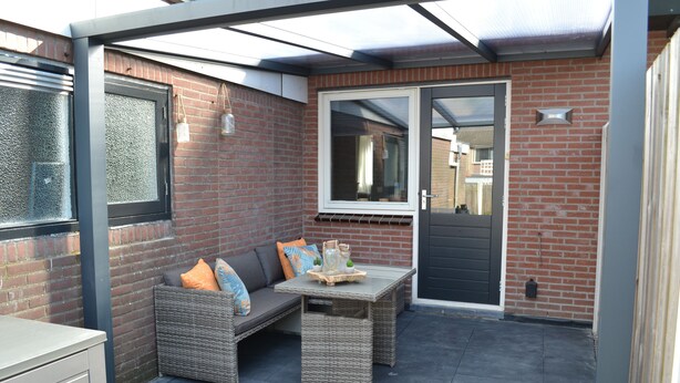A patio area with a wicker sofa, a small table, and a glass door. - Apartment in the middle of the center of Oostkapelle an apartment with charm (Oostkapelle)