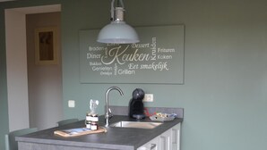 A modern kitchen with a grey island, a hanging pendant light, and a wall-mounted sign listing food items. - Apartment in the middle of the center of Oostkapelle an apartment with charm (Oostkapelle)