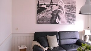 A living room with a black leather sofa, a framed photograph of a stormy sea, and a white lamp. - Apartment in the middle of the center of Oostkapelle an apartment with charm (Oostkapelle)