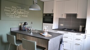 A modern kitchen with a central island, bar stools, a built-in oven, and a word cloud on the wall. - Apartment in the middle of the center of Oostkapelle an apartment with charm (Oostkapelle)