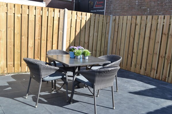 An outdoor patio with a table and four chairs, a potted plant, and a wooden fence.