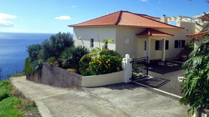 Ein Küstenhaus mit rotem Ziegeldach, befestigter Auffahrt und Garten mit gelben Blumen.