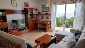 Ein Wohnzimmer mit Fernseher, Sofa und Balkon mit Blick.