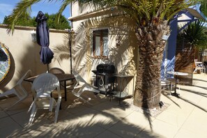 Eine Terrasse im Freien mit Tisch, Stühlen, einem Grill und einer Palme.