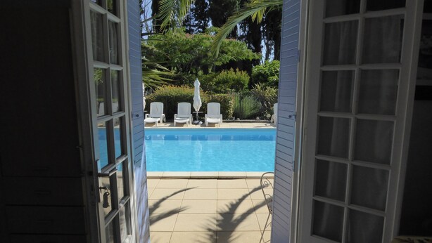 Une porte ouverte donne sur un espace piscine, où se trouvent des chaises et des parasols blancs.