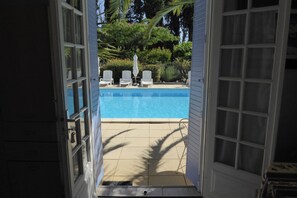 Eine offene Tür, die zu einem Poolbereich mit weißen Stühlen und einer Palme führt.