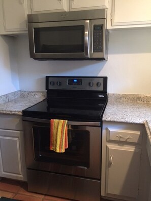 Una cocina con microondas de acero inoxidable, horno y placa de cocción negra.