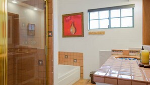 Un baño con cabina de ducha de vidrio, bañera, ventana y zona de lavamanos con azulejos.
