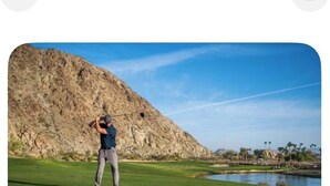 Una persona en un campo de golf con una gran formación rocosa al fondo.