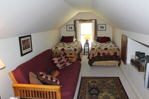 A small, cozy room with two beds, a red sofa, a wooden chair, and a patterned rug.