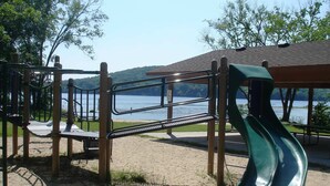 Une aire de jeux avec un toboggan et des structures d’escalade, située près d’un lac.